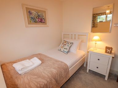 A single bed with a beige blanket and white towels on it next to a white nightstand with a lamp and a wicker basket at Highfold in Ambleside