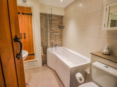 A bathroom with a bathtub shower combination a toilet a wooden door and tiled walls at Highfold in Ambleside