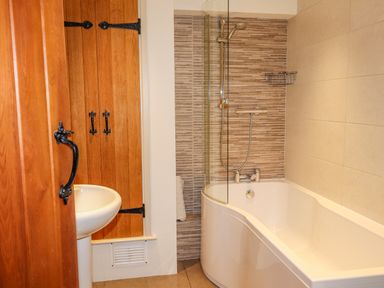 A bathroom with a wooden door and cabinets a white sink and a bathtub with a shower at Highfold in Ambleside
