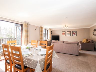 A dining table set with six chairs and bowls in a living room with sofas and a TV at Ghyll View in Ambleside
