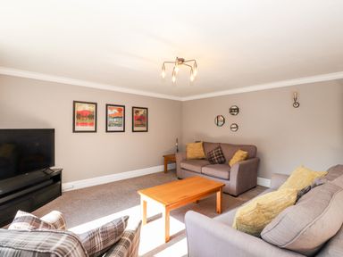 A living room with sofas cushions a wooden coffee table TV and framed pictures on the wall at Ghyll View in Ambleside
