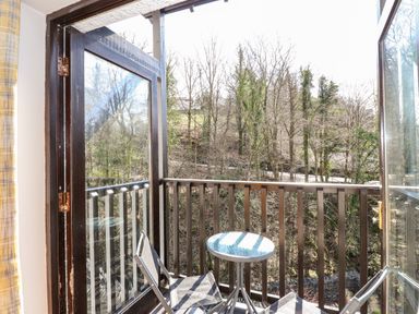 A balcony with a small round table and two folding chairs overlooking trees at Ghyll View in Ambleside