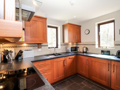 A kitchen with wooden cabinets black countertops a sink microwave toaster kettle and two windows at Ghyll View Ambleside