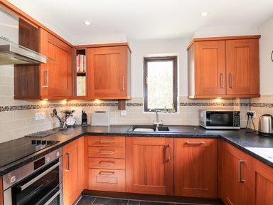 A kitchen with wooden cabinets a black countertop a window a microwave oven and a kettle at Ghyll View in Ambleside