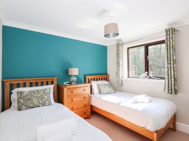A bedroom with two single beds a wooden dresser and a window with patterned curtains at Ghyll View in Ambleside