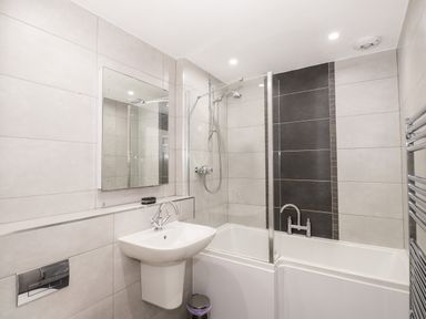 A bathroom with a pedestal sink a wall mirror a bathtub with shower and a glass shower screen at Ghyll View in Ambleside