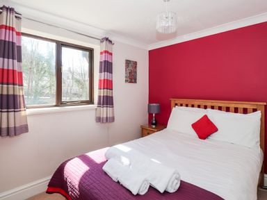 A bedroom with a double bed against a red wall and a window with striped curtains at Ghyll View in Ambleside