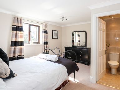 A bedroom with a bed, dresser with mirror, window with curtains, and an ensuite bathroom at Ghyll View in Ambleside