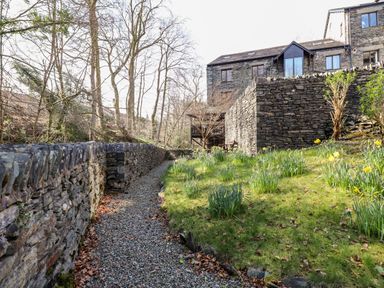A stone pathway beside a grass lawn with flowers and a stone building in the background at Ghyll View in Ambleside