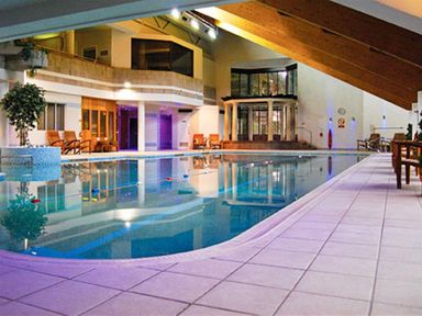 An indoor swimming pool with chairs and plants around and wooden beams on the ceiling at Rawfell Great Langdale
