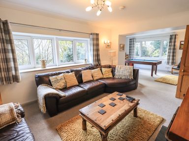 A living room with a leather sectional sofa and wooden coffee table beside a game room with a pool table at Rawfell in Great Langdale