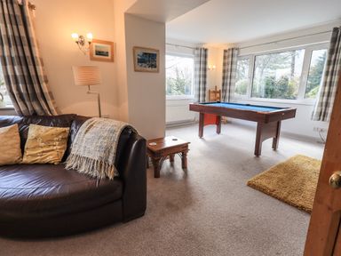 A living room with a brown leather sofa and cushions a pool table near large windows and a small wooden side table at Rawfell in Great Langdale