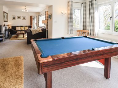 A room with a pool table a wooden chair a living area with sofas a coffee table and wall paintings at Rawfell in Great Langdale