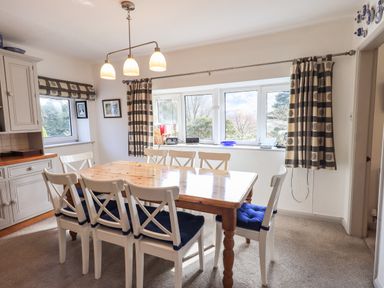 A dining room with a wooden table and eight white chairs with blue cushions at Rawfell in Great Langdale