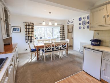 A dining area with a wooden table and white chairs with blue cushions in a kitchen with white cabinets and blue decorative plates on the wall at Rawfell in Great Langdale