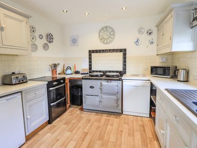 A kitchen with white cabinets wooden flooring a stove oven dishwasher microwave and toaster at Rawfell in Great Langdale