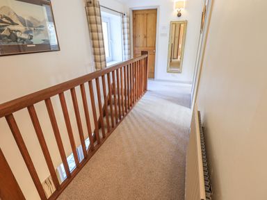 A carpeted hallway with wooden railing window wooden door and a mirror at Rawfell in Great Langdale