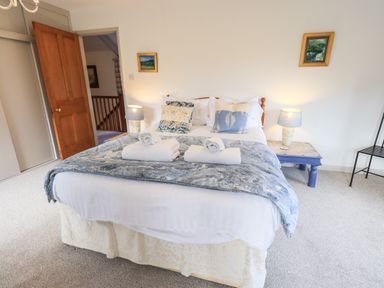 A bedroom with a double bed with pillows and rolled towels bedside tables with lamps and a wooden door open at Rawfell in Great Langdale