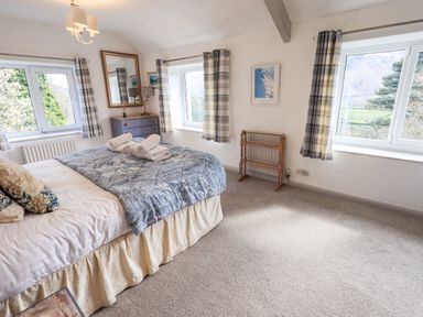A bedroom with a double bed and blue quilt near windows with plaid curtains at Rawfell in Great Langdale