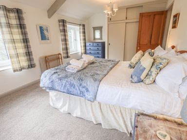 A bedroom with a bed dressed with pillows and folded towels near windows with plaid curtains at Rawfell in Great Langdale