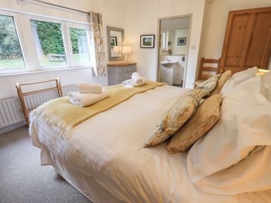 A bedroom with a bed with pillows and folded towels near a window and a door leading to a bathroom at Rawfell in Great Langdale