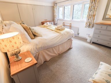 A bedroom with a bed with pillows and towels bedside tables lamps a chest of drawers and a window with curtains at Rawfell in Great Langdale
