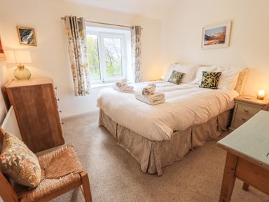 A bedroom with a double bed with pillows and towels by a window with patterned curtains at Rawfell in Great Langdale