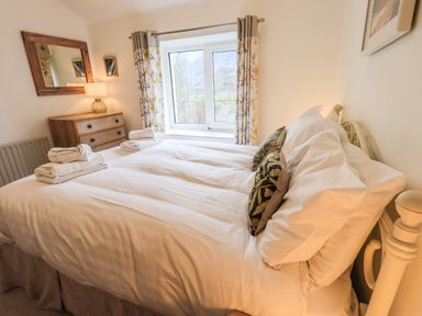 A bedroom with a bed with white linens pillows and folded towels a wooden dresser a mirror and a window with floral curtains at Rawfell in Great Langdale