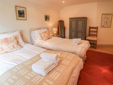 A bedroom with two single beds with towels on them a wooden wardrobe a chair and framed pictures on the walls at Rawfell in Great Langdale