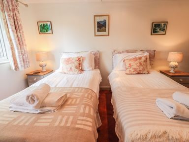 A bedroom with two single beds lamps on wooden bedside tables and paintings on the wall at Rawfell in Great Langdale