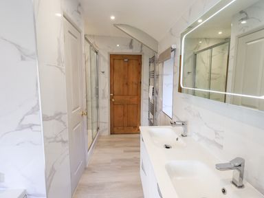 A bathroom with double sinks a lighted mirror a shower with glass doors and wooden doors at Rawfell in Great Langdale