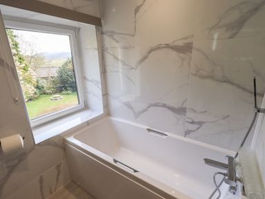 A bathroom with a bathtub next to a window showing a garden outside at Rawfell Great Langdale