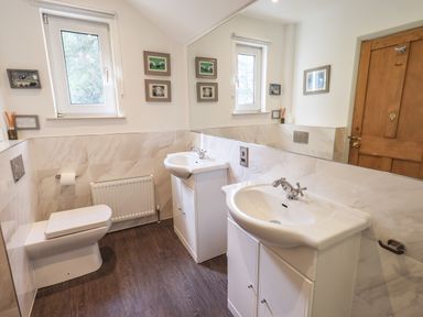 A bathroom with two sinks a toilet a wooden door and framed pictures on the wall at Rawfell in Great Langdale