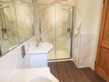 A bathroom with a sink, shower enclosure, towel on wall, wooden door, and dark wooden floor at Rawfell in Great Langdale