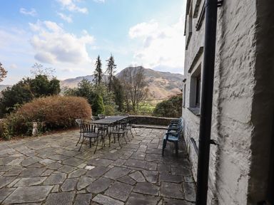 An outdoor patio with stone flooring a black metal table and chairs and green plastic chairs against a white stone wall at Rawfell in Great Langdale