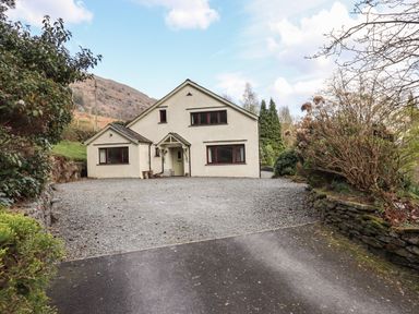 A house with a gravel driveway and surrounding trees and bushes at Rawfell in Great Langdale