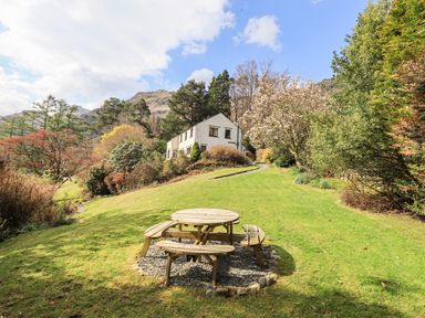 A wooden picnic table on a grass lawn with a two-story house and various trees in the background at Rawfell in Great Langdale
