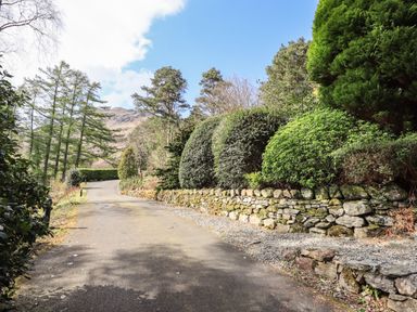 A winding paved driveway with trimmed bushes and a stone wall at Rawfell in Great Langdale