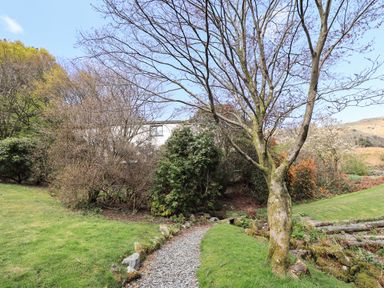 A garden path with grass trees and shrubs near a white house at Rawfell in Great Langdale