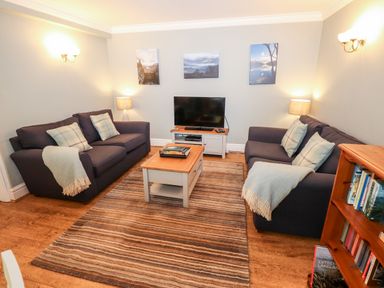 A living room with two sofas a wooden coffee table a television and a bookcase at Babbling Brook in Ambleside