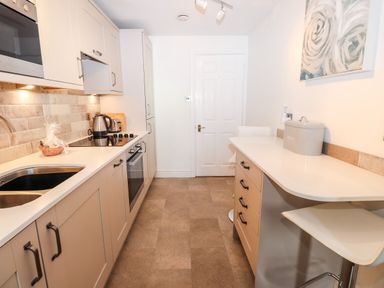 A kitchen with white cabinets a sink a built in oven a countertop and bar stools at Babbling Brook in Ambleside