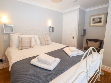 A bedroom with a white metal bed frame a gray blanket and neatly folded white towels at Babbling Brook in Ambleside