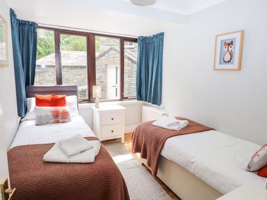 A bedroom with two single beds a nightstand between the beds and a window with blue curtains at Babbling Brook in Ambleside