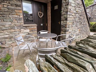An outdoor seating area with a round metal table and four metal chairs in front of stone buildings at Babbling Brook in Ambleside