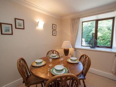 A dining area with a round wooden table set for four next to a window with a vase on the sill at Over Ghyll in Ambleside