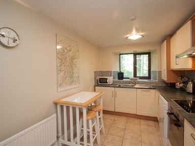 A kitchen with a small table and two stools a microwave on the counter a window above sink and tiled floor at Over Ghyll Ambleside