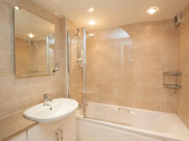 A bathroom with a sink countertop a mirror a bathtub with a shower and glass screen at Over Ghyll in Ambleside