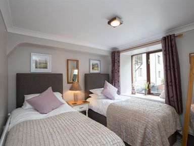 A bedroom with two single beds a bedside table with a lamp and a window with curtains at Over Ghyll in Ambleside