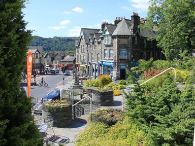 A street with stone buildings shops and greenery in a town with people walking and cycling at Over Ghyll Ambleside