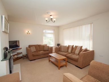 A living room with brown sofas a wooden coffee table a television and vertical blinds on windows at Bield How in Ambleside